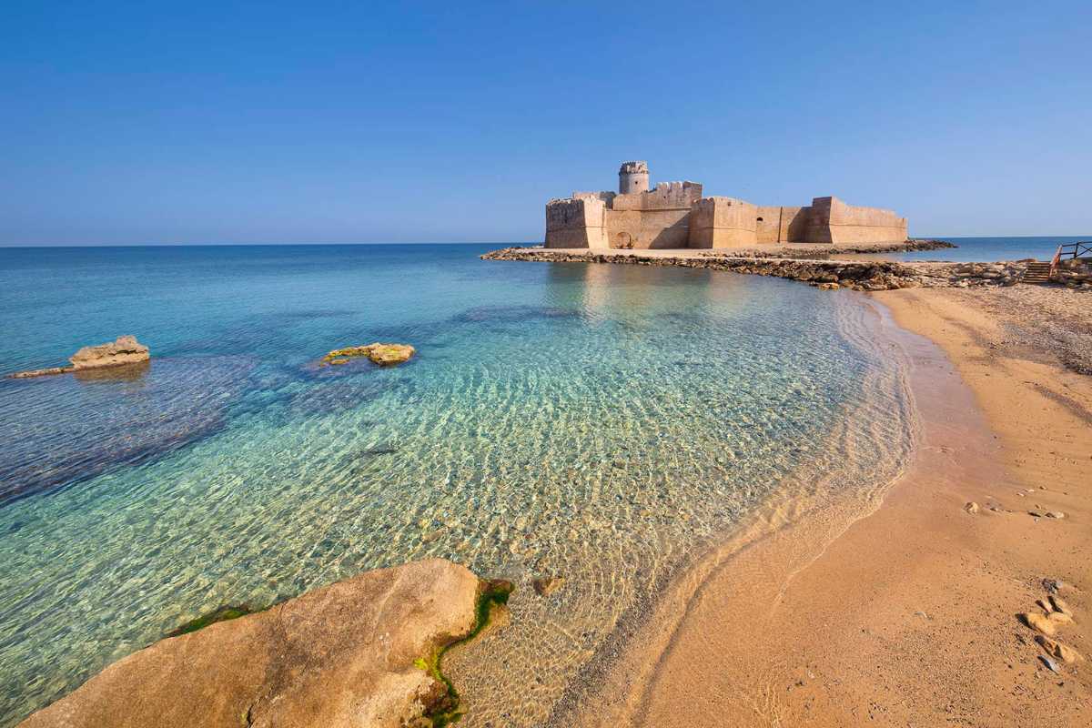 Fortezza Aragonese a Le Castella vista dal mare, con spiaggia e cielo azzurro